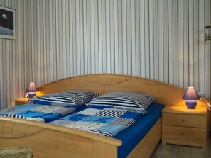 Een bed met een houten hoofdbord, gestreept beddengoed, twee bedlampjes en een muur met verticale strepen.
