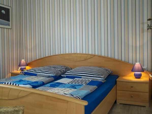 A bed with a wooden headboard, striped bedding, two bedside lamps, and a wall with vertical stripes. - Bungalow Nele - Bungalow (Göhren-Lebbin)