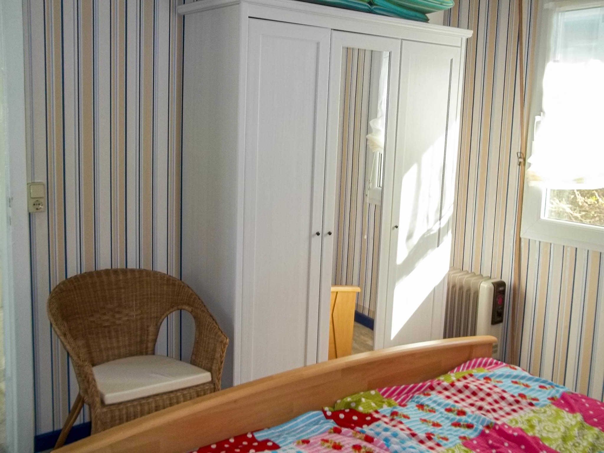 A bedroom with a bed, a wicker chair, a wardrobe, and a window.