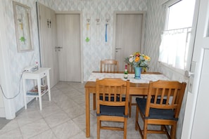 A dining area with a table, chairs, a small white table with a radio, and a window with a view.
