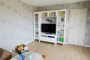 Un salon avec un téléviseur, un meuble de rangement blanc et une porte.