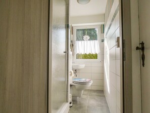 Un baño estrecho con inodoro, lavabo y ventana con cortina.