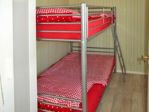 Un lit superposé avec une literie à carreaux rouges et blancs, une échelle en métal et un papier peint à rayures en arrière-plan.