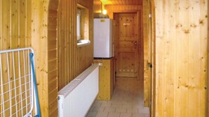 Ein schmaler Holzkorridor mit einer weißen Heizung, einem blauen Metallgitter und einem weißen Kühlschrank.
