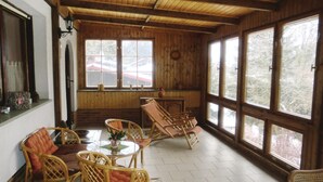 Ein Zimmer mit Holzwänden, großen Fenstern, Korbmöbeln und einem kleinen Tisch mit einer Vase.