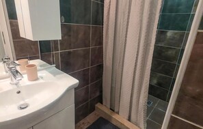 Une salle de bain avec un lavabo blanc, deux tasses beiges, un miroir et des murs recouverts de carreaux foncés.