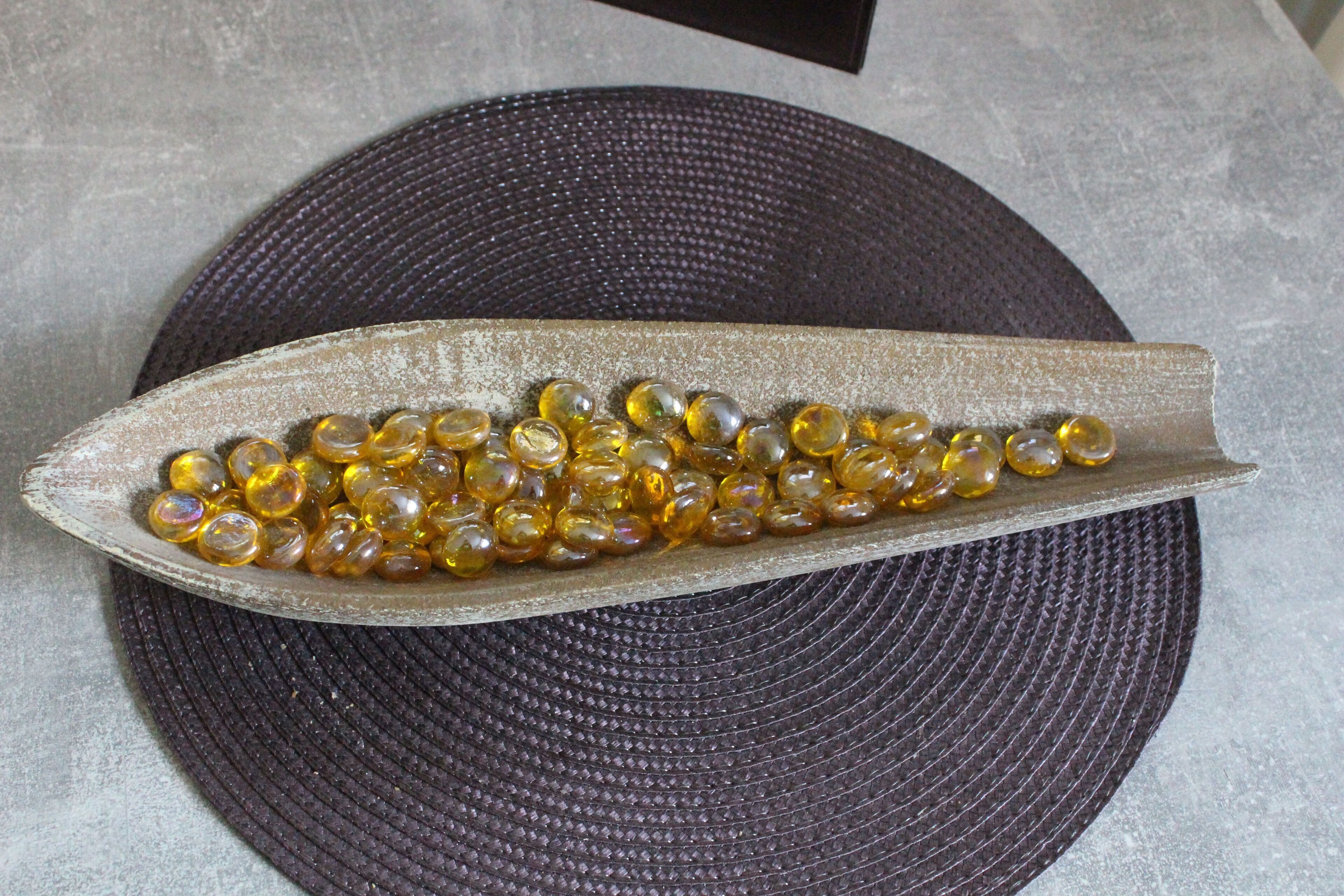 A dark textured circular mat with a metallic object containing yellowish beads.