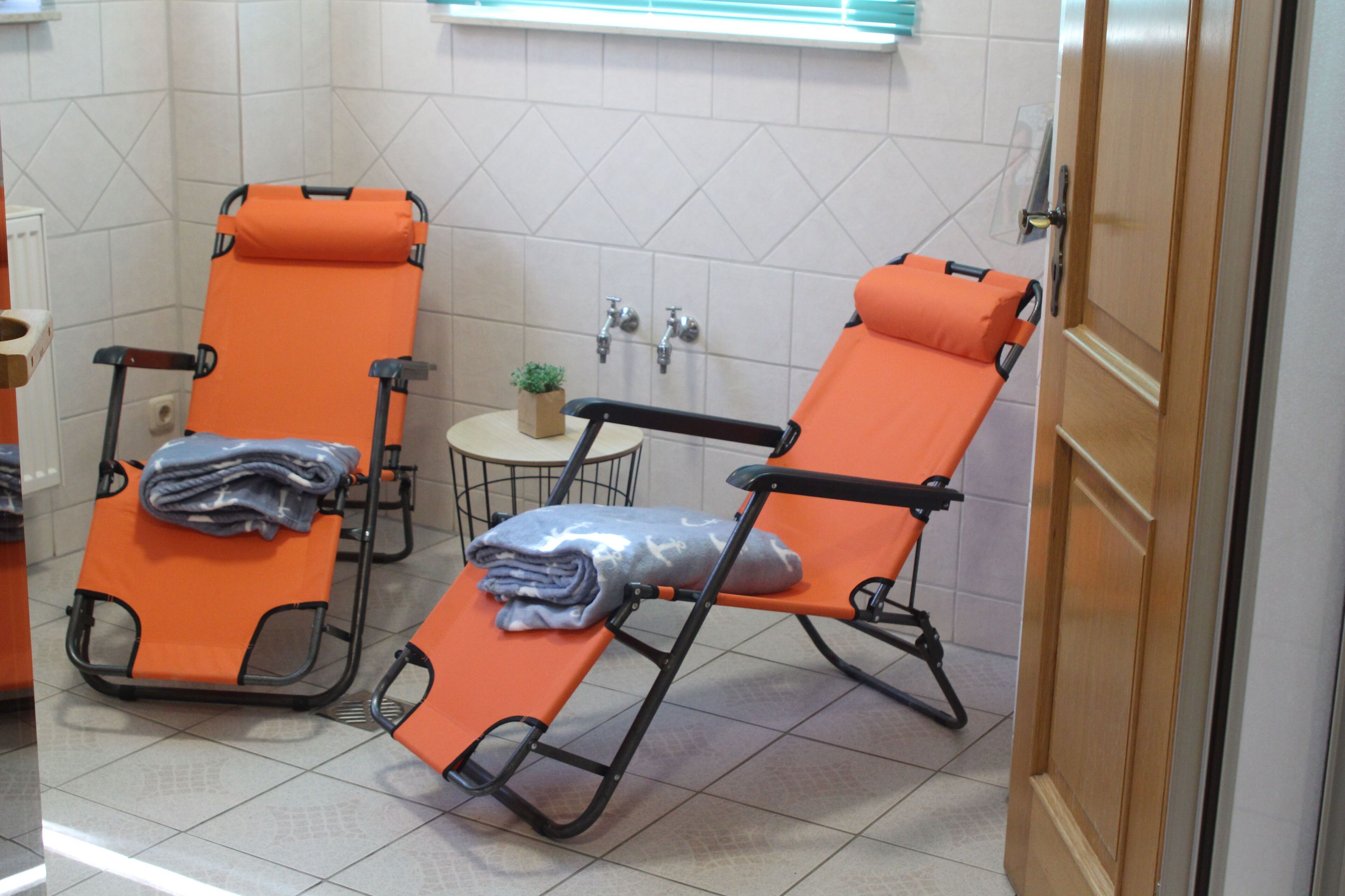 Une pièce avec deux fauteuils orange inclinables, une petite table sur laquelle se trouve une plante, et une porte en bois.