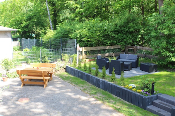 Un patio con una mesa y bancos de madera, rodeado de un jardín con plantas y flores.