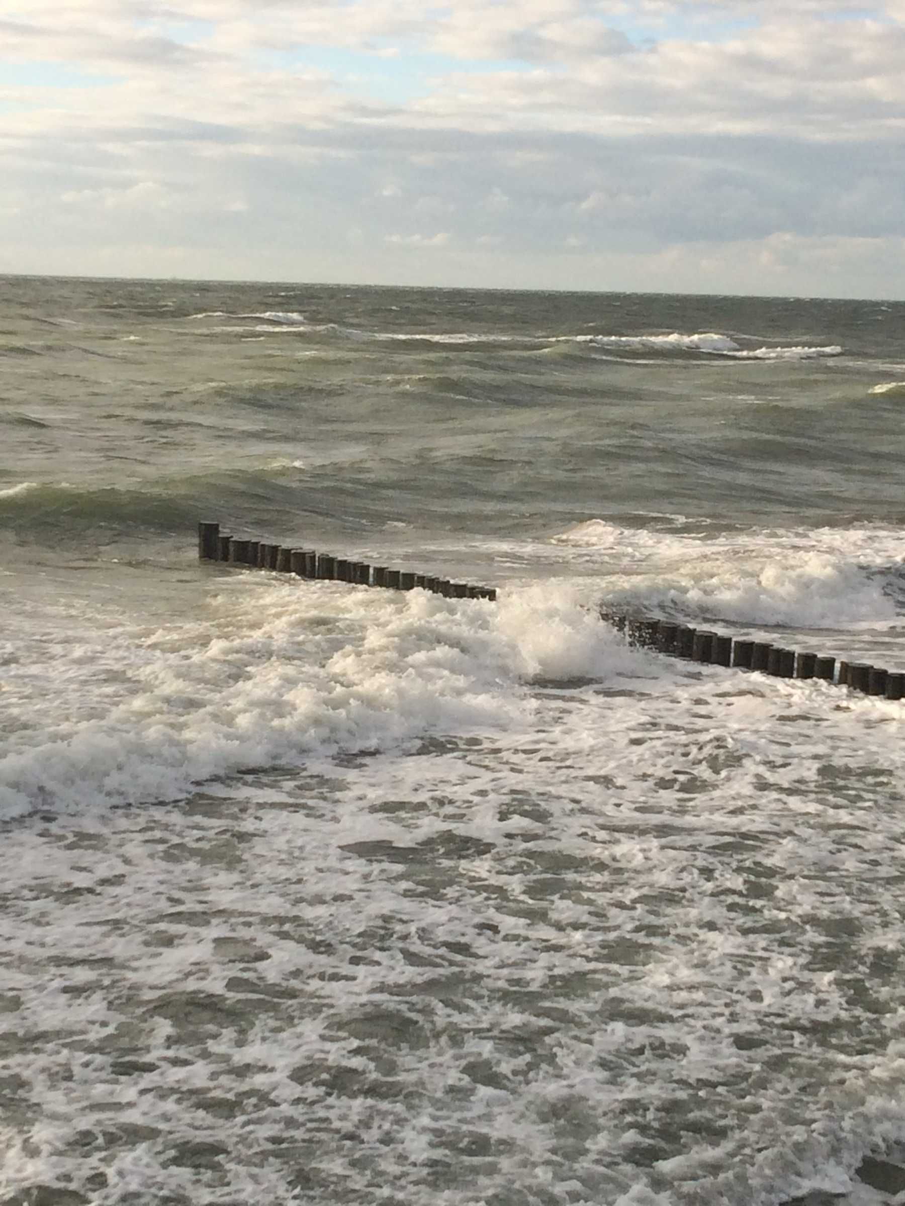 Blick auf das Meer mit brechenden Wellen an einer Betonmauer.