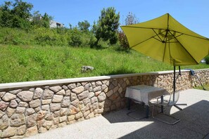 Un patio con un muro de piedra, una mesa con mantel y un paraguas amarillo.