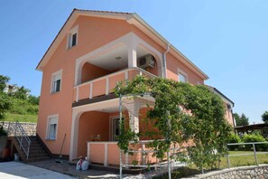 A two-story building with a balcony, a staircase, and a garden area.