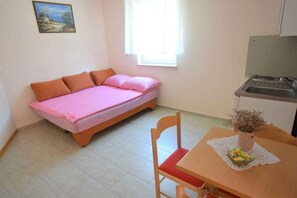 A small room with a bed, a table with a vase, a chair, and a window.