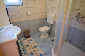 A bathroom with a sink, toilet, shower, and patterned floor mat.