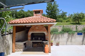 An outdoor brick oven with a tiled roof, a stone wall, and potted plants.