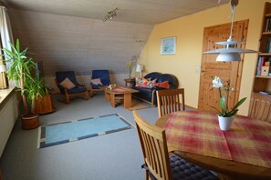 A cozy living room with a wooden ceiling, a dining table with a plaid tablecloth, and a bookshelf.