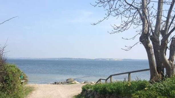 Een grindpad dat naar een strand leidt, met een houten leuning en een stenen muur aan één kant.