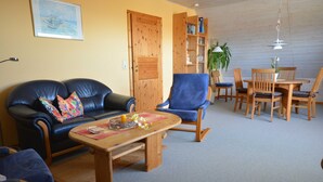 Een woonkamer met een bank, fauteuils, een salontafel en een eethoek met een tafel en stoelen.