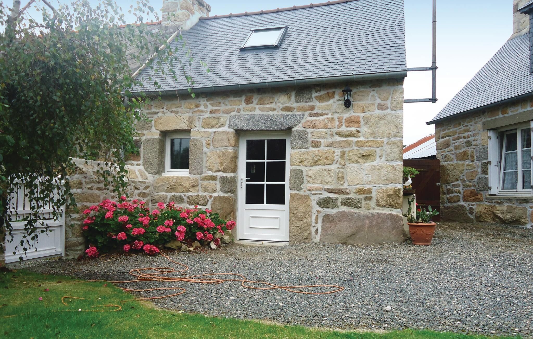 Ein Steinhäuschen mit einer weißen Tür, einem kleinen Fenster und einem Garten mit rosa Blumen.