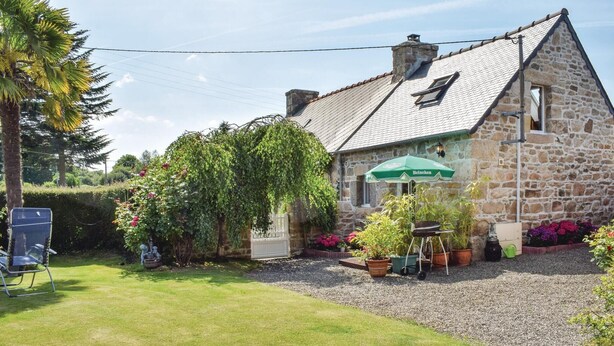 Een gebouw van steen met een schuin dak, een groene parasol en een barbecue op de voortuin.