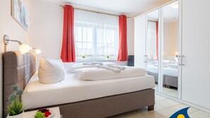 A modern hotel room with a large bed, a bedside table with a lamp, a small potted plant, and a plate of fruit. - Apartment (ap.) Whg. 01 Gartenstraße - Garden 01 (Heringsdorf)
