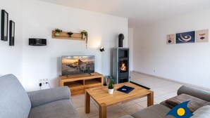 A modern living room with a sofa, coffee table, TV, fireplace, and wall-mounted shelf with plants. - Apartment (ap.) Whg. 01 Gartenstraße - Garden 01 (Heringsdorf)