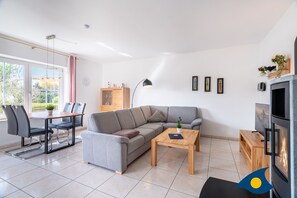A modern living room with a grey sectional sofa, a wooden coffee table, a dining table with chairs, a TV, and a fireplace. - Apartment (ap.) Whg. 01 Gartenstraße - Garden 01 (Heringsdorf)