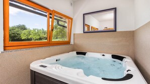 A bathroom with a hot tub, a window with a view of greenery, and a mirror on the wall. - Beautiful home in Lukovdol with sauna (Lukovdol)