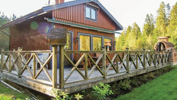 Eine Holzhütte mit Balkon, umgeben von Grün und einer kleinen Brücke.