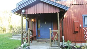 Eine hölzerne Veranda mit einer blauen Tür, einer kleinen Sitzgelegenheit im Freien und einem Garten mit Pflanzen.