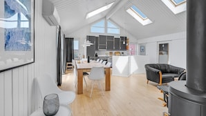 A modern loft with a high ceiling, skylights, a dining area with a wooden table and chairs, a black leather sofa, and a kitchen with dark cabinets. - Gorgeous home in Thisted with sauna (Thisted)