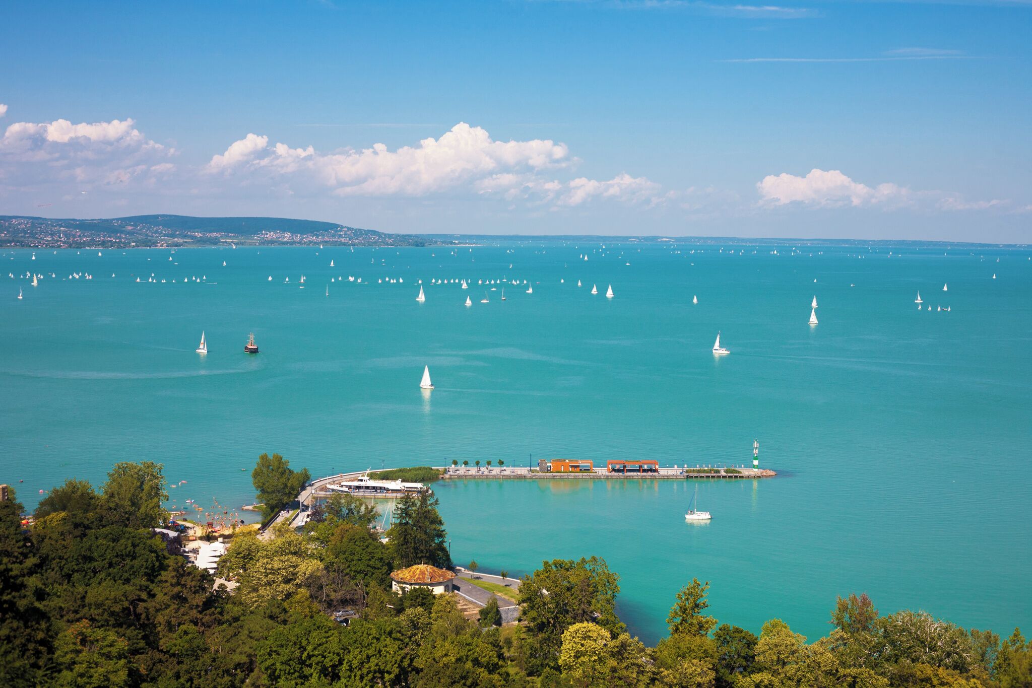 A coastal town with a marina filled with sailboats, a lighthouse, and a pier with buildings.
