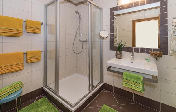 A modern bathroom with a glass-enclosed shower, a sink with a mirror, and multiple towels on towel racks.