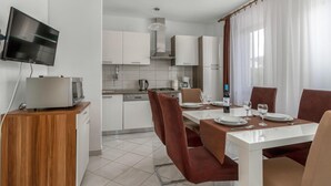 A modern kitchen with white cabinets, a microwave, and a dining area with a white table and brown chairs. - 3 bedroom beach front apartment in Jadranovo (Jadranovo)