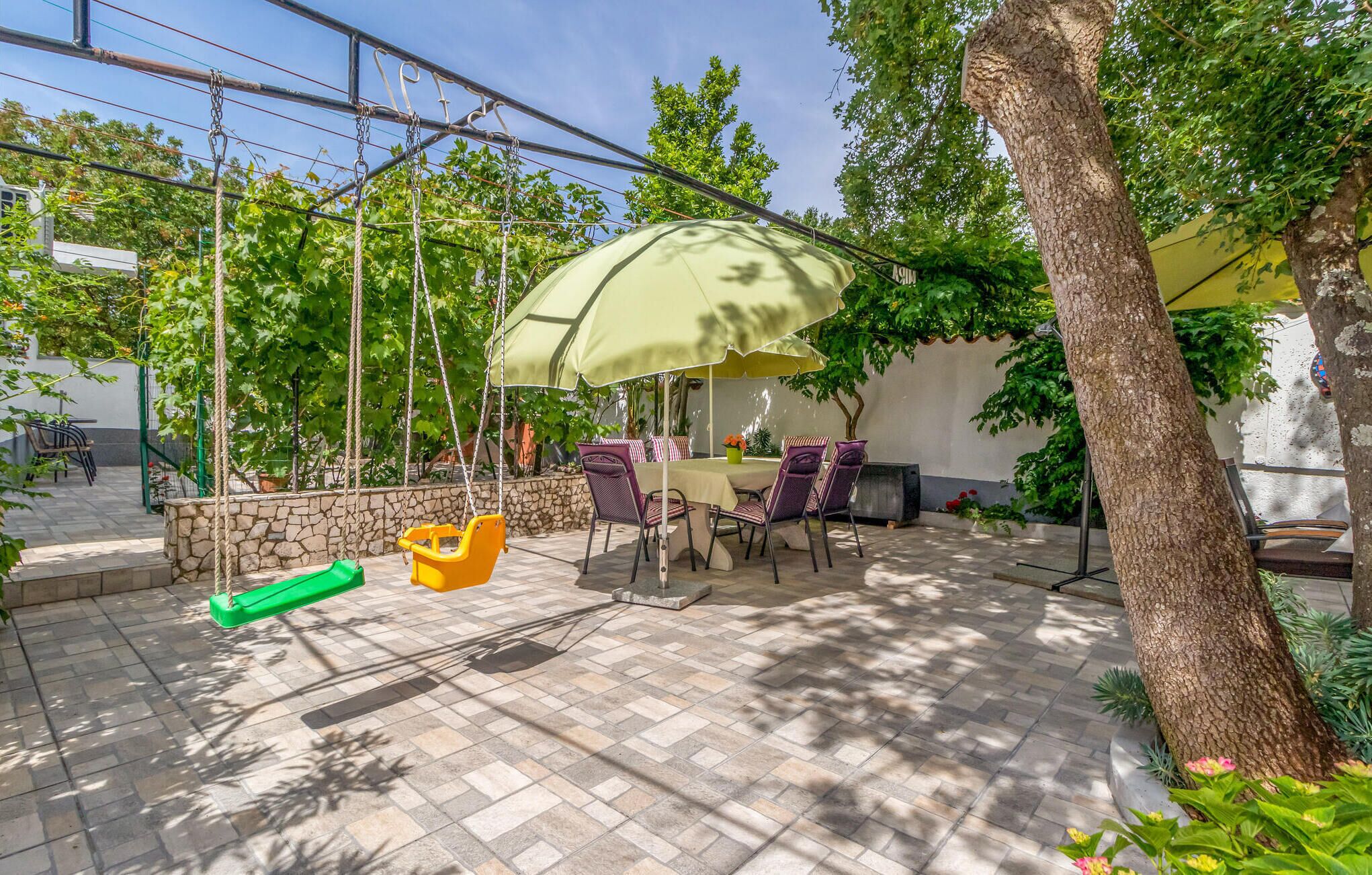A patio area with a table and chairs under a canopy, surrounded by stone walls and greenery.