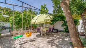 A patio area with a table and chairs under a canopy, surrounded by stone walls and greenery. - 3 bedroom beach front apartment in Jadranovo (Jadranovo)