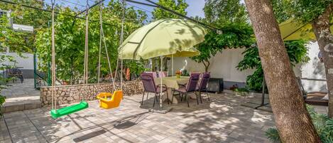 A patio area with a table and chairs under a canopy, surrounded by stone walls and greenery.