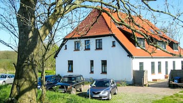 A white building with a red roof, parked cars, and a tree in the foreground.
