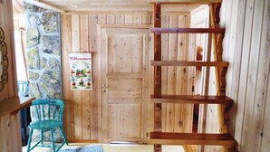 Interior de madera con pared de piedra, una puerta, una silla azul y una estantería de madera.