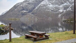 Una mesa de picnic de madera junto a un lago tranquilo con montañas nevadas al fondo.