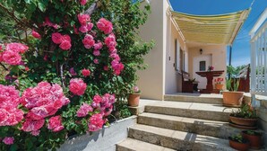 Eine Treppe führt zu einem Gebäude mit überdachter Eingangspartei, umgeben von Topfpflanzen und blühenden rosa Blumen.