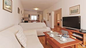 Una sala de estar con un sofá, una mesa de centro con tazas y una revista, un televisor y una cocina al fondo.