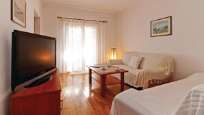 Habitación de hotel con televisión de pantalla plana sobre un soporte de madera, un sofá, una mesita con lámpara y una cama con cubrecama blanco.