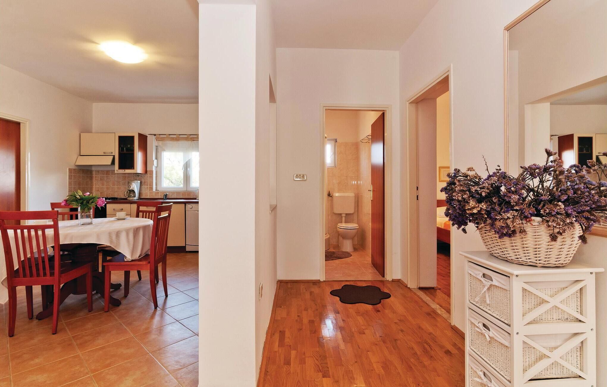 A modern kitchen with white cabinets, a dining area with wooden chairs, and a hallway leading to a bathroom.