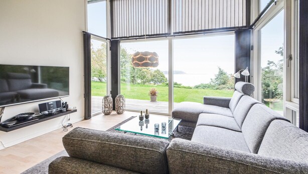 A modern living room with a large TV, comfortable grey sofa, and a glass coffee table. - 3 bedroom cozy home in Roslev (Roslev)