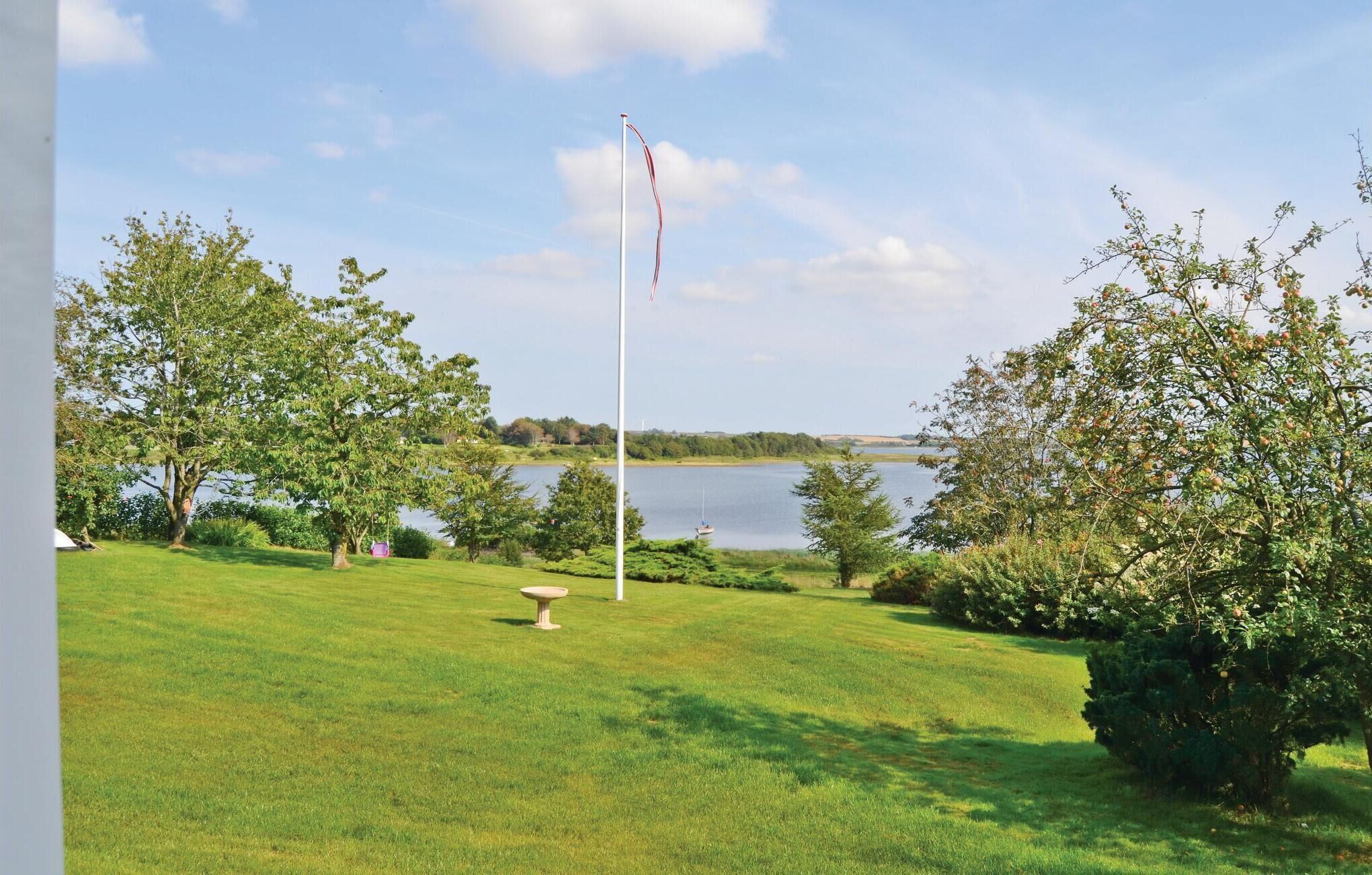 A grassy area with a flagpole, trees, and a body of water in the background.