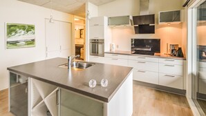 A modern kitchen with a central island, stainless steel appliances, and white cabinetry. - 3 bedroom cozy home in Roslev (Roslev)