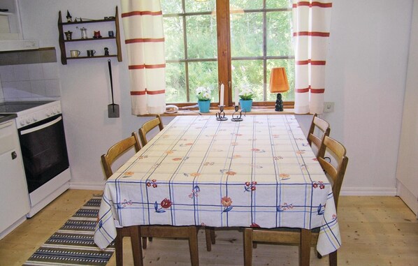 Un coin repas avec une table dressée pour quatre personnes, une fenêtre avec des rideaux, un poêle et une étagère contenant des ustensiles de cuisine.