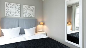 Un letto rifatto con lenzuola bianche, una testiera grigia e due pannelli decorativi fissati al muro.