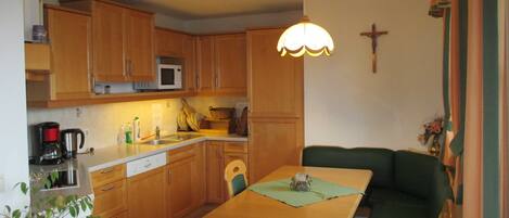 A compact kitchen with wooden cabinets, a dining table with chairs, a small sink, and a cross on the wall.